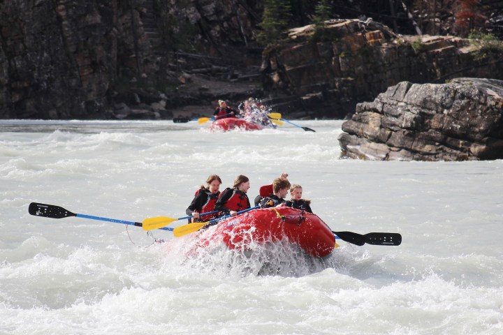 People whitewater rafting on a river with two red rafts navigating a rapid.