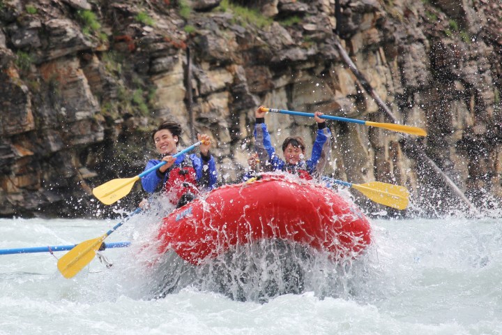 Two people rafting on a river, holding paddles, surrounded by splashing water.