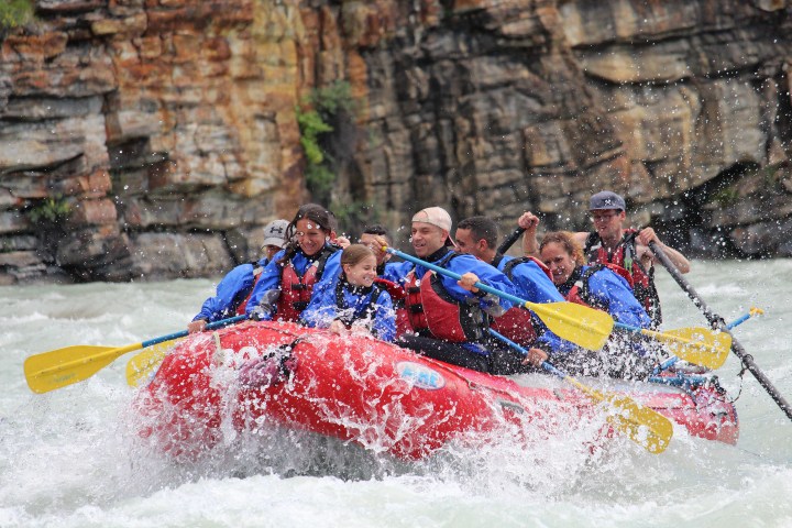 Group of people whitewater rafting in a red raft on a rocky river.