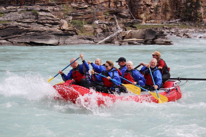 Group in red raft whitewater rafting with paddles on a rocky river.