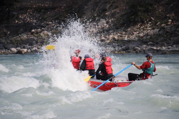 Group in red boat navigating rapids with water splashing around.