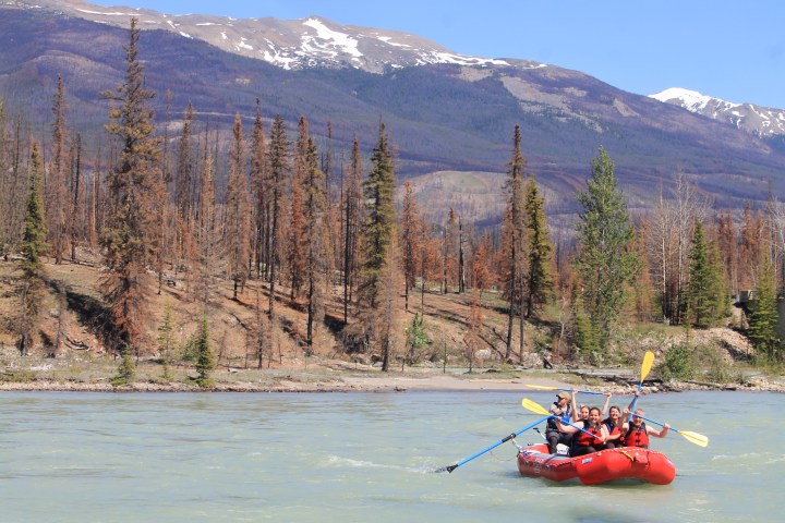 Group rafting on a river with mountain and forest backdrop.