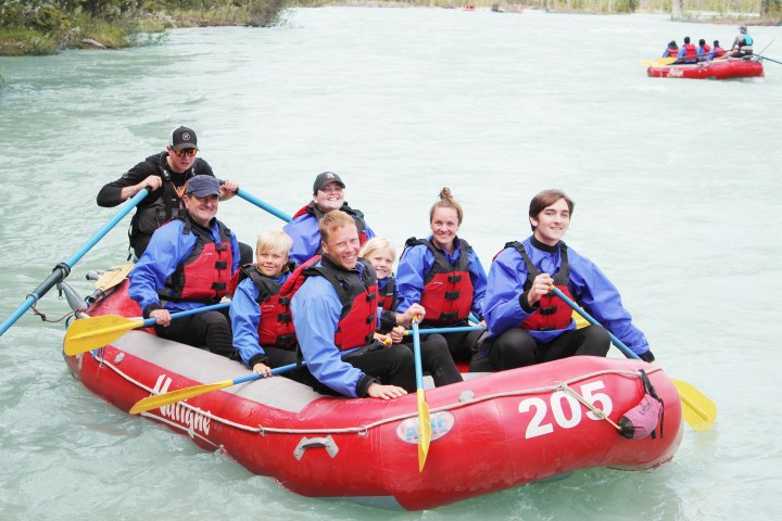 Group of eight people in life jackets rafting on a river in a red inflatable boat.
