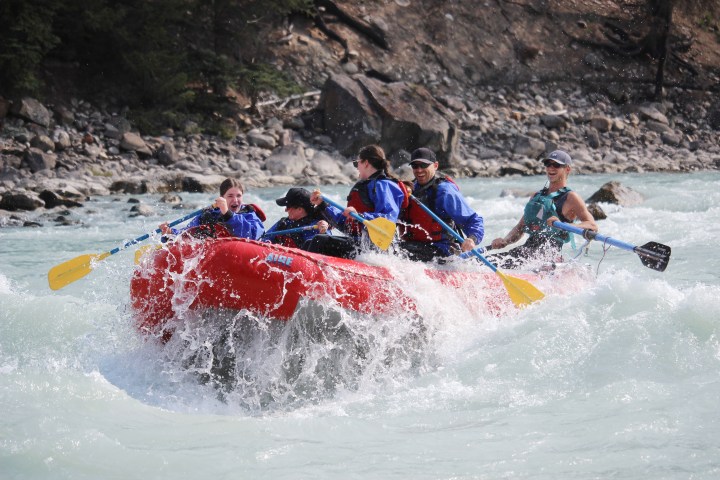 Group whitewater rafting in a red inflatable boat on a turbulent river.