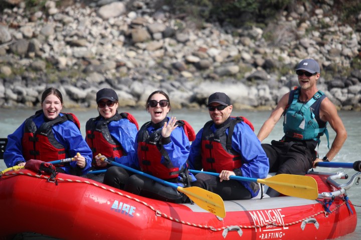Group of five people in life vests enjoying a rafting adventure on a river.