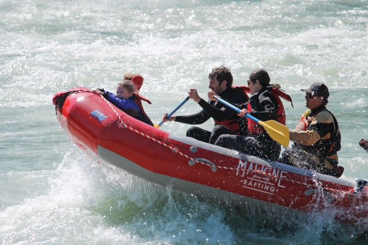 Group rafting in red inflatable boat on choppy river water.